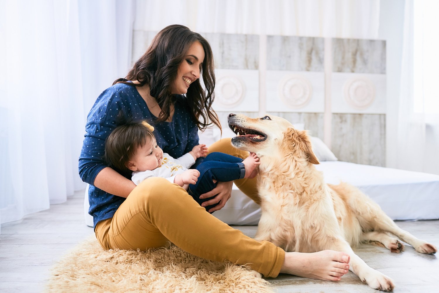 Woman playing with a baby and a golden retriever on a rug