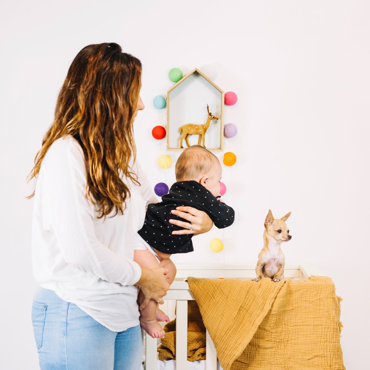 Woman holding a baby next to a small chihuahua in a bright nursery
