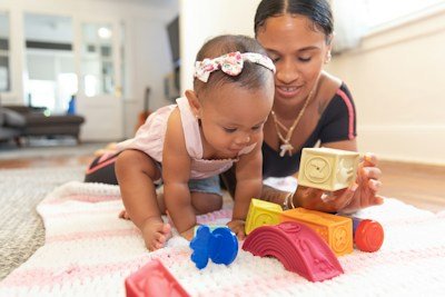 Baby playing with toy blocks next to a smiling woman